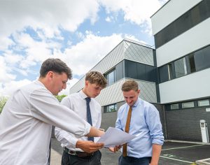 Three project team members review construction plans outside the new UEA School of Anatomy extension, standing beside the modern façade of the Edith Cavell Building during a site inspection.