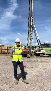 R G Carter team member on site at the Queen Elizabeth Hospital multi-storey car park project in King’s Lynn, standing in front of a continuous flight auger (CFA) piling rig operated by GM Piling.