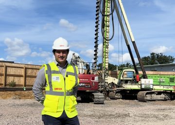R G Carter team member on site at the Queen Elizabeth Hospital multi-storey car park project in King’s Lynn, standing in front of a continuous flight auger (CFA) piling rig operated by GM Piling.